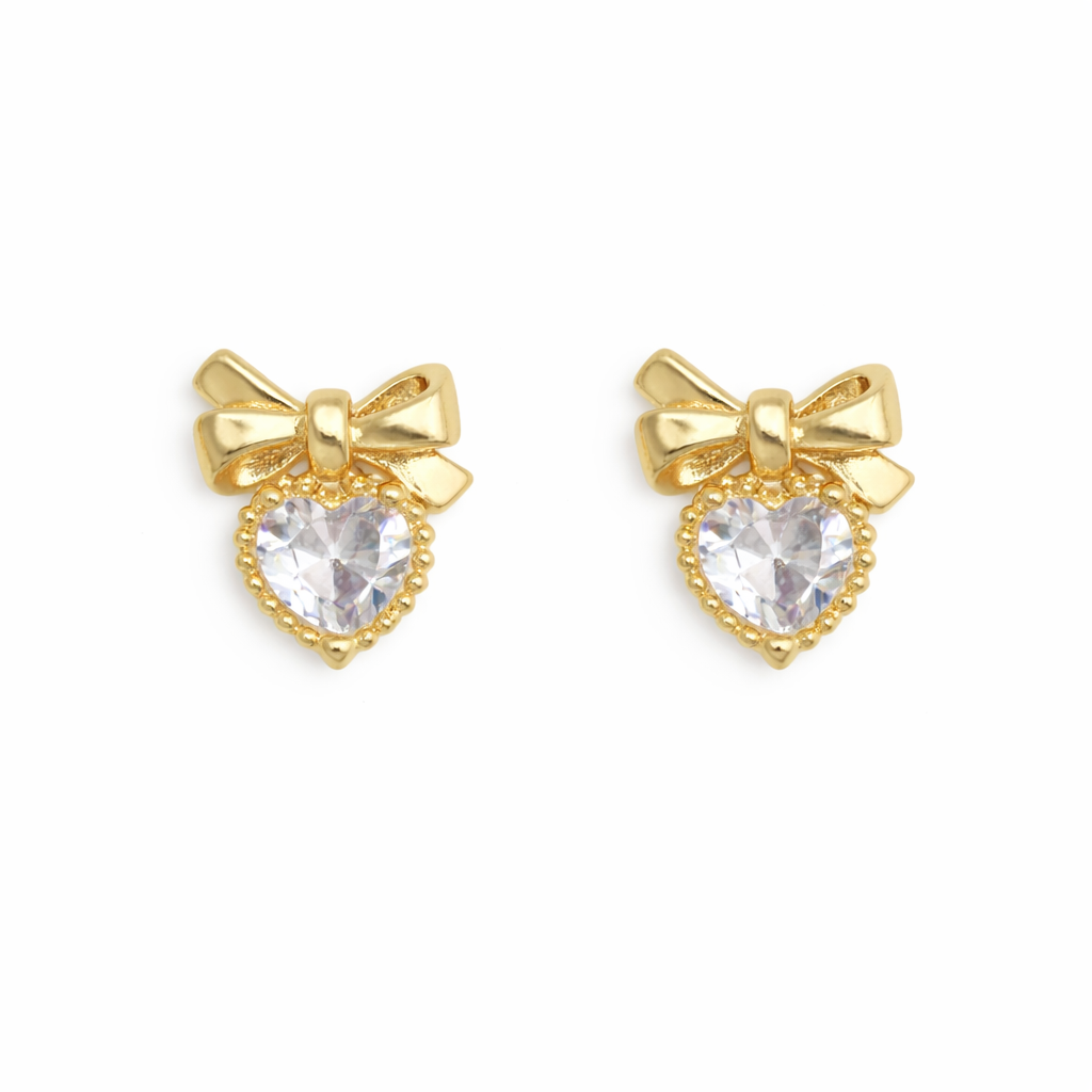 Gold bow-shaped nail charms with clear heart stones on a white background