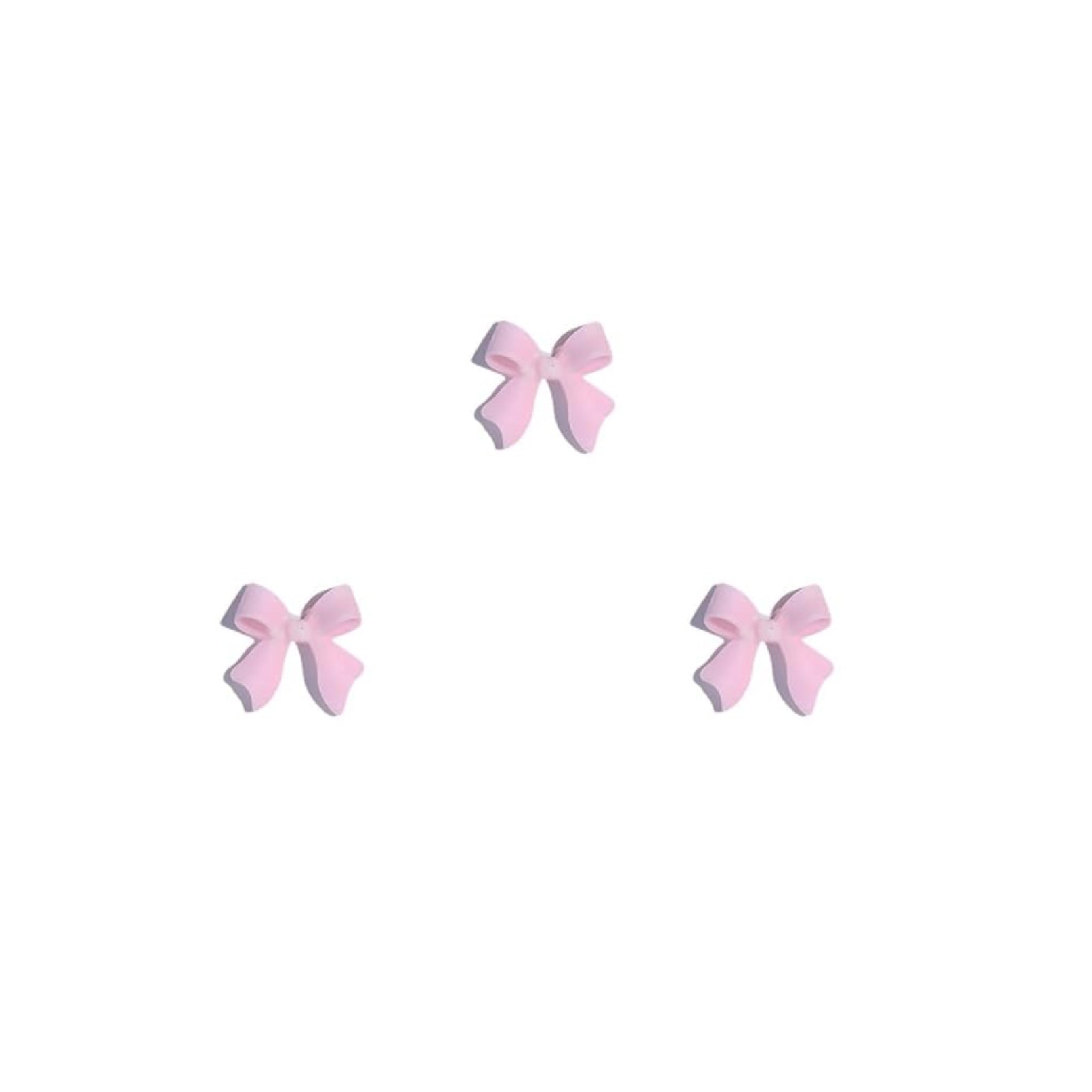 Set of three pink bow-shaped nail charms on a white background