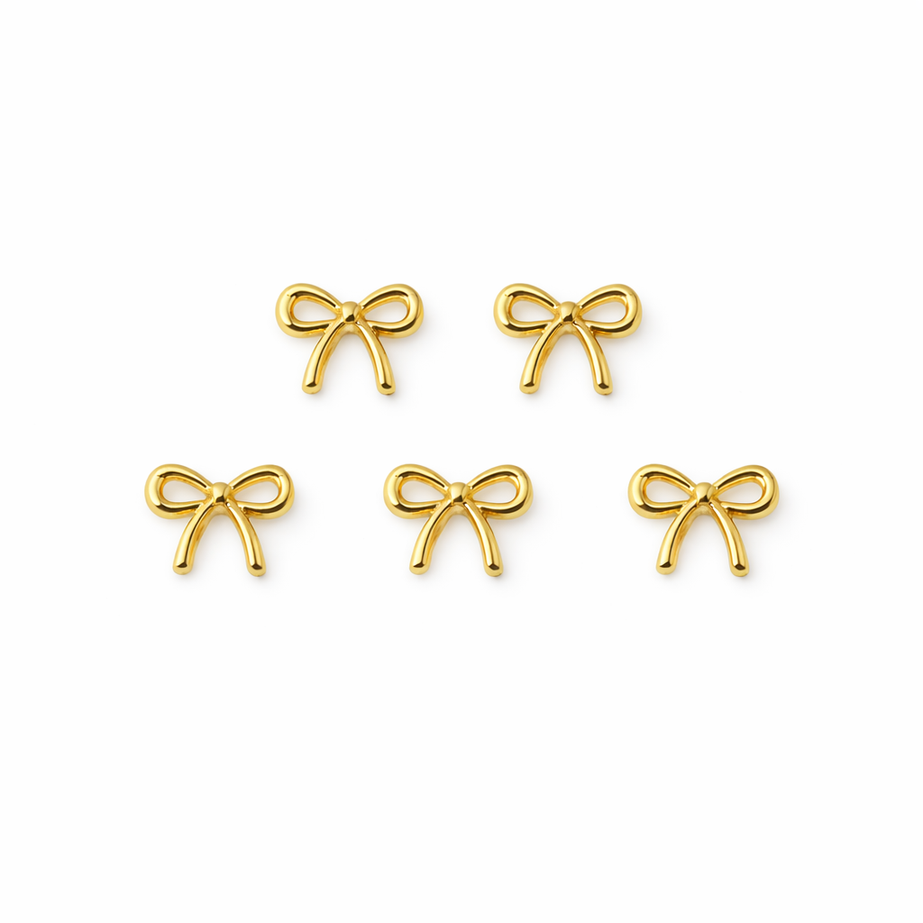 Set of gold bow-shaped nail charms on a white background